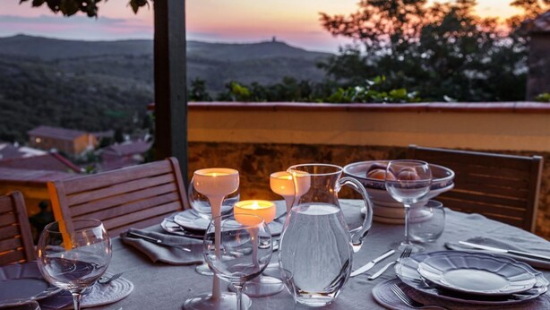 Une table dressée pour le dîner, avec vue sur un coucher de soleil se reflétant sur un paysage montagneux.