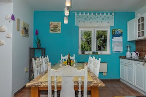 A dining area with a marble table, white chairs, and a window with star-patterned curtains. - Apartment Barbara (Crikvenica)