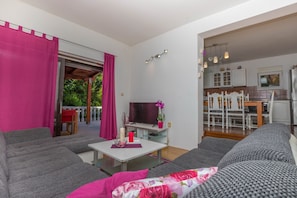 A living room with a sofa, a TV, and a dining area with a table and chairs. - Apartment Barbara (Crikvenica)