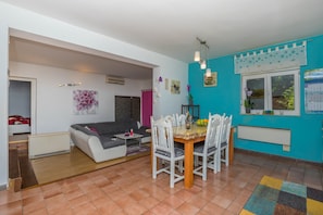 A dining area with a table and chairs, a sofa, and a window with a view of greenery. - Apartment Barbara (Crikvenica)
