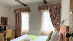 A hotel room with a bed, a desk, a chair, a television, and a window with curtains. - Ye Olde House (Shepperton)