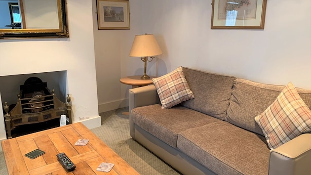 A living room with a sofa, a wooden coffee table, a lamp, and a fireplace. - Ye Olde House (Shepperton)