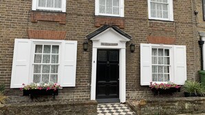 A two-story brick building with white-framed windows and shutters, a black front door, and a sign that reads "Ye Olde House". - Ye Olde House (Shepperton)