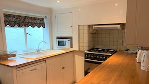 A kitchen with white cabinets, a stove, a microwave, and a sink. - Ye Olde House (Shepperton)