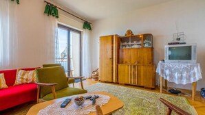 A living room with a red sofa, green armchairs, a wooden cabinet, a television, and a table with a lace tablecloth. - Apartment Ivka (Crikvenica)
