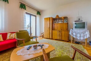 Ein Wohnzimmer mit einem roten Sofa, grünen Sesseln, einer Holzkabine, einem Fernseher und einem Tisch mit einer Spitzenleinentischdecke.