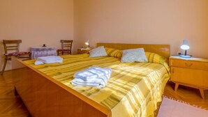 A bedroom with a wooden bed, two bedside tables, a chair, and a small table. - Apartment Ivka (Crikvenica)