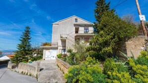 A two-story building with a balcony on the second floor, surrounded by greenery and a clear blue sky. - Apartment Ivka (Crikvenica)