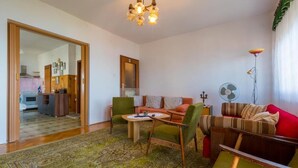 A living room with a sofa, chairs, a coffee table, and a rug. There is a kitchen visible through an open door. - Apartment Ivka (Crikvenica)