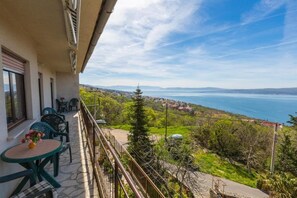 A balcony with a view of a coastal landscape, including a body of water and distant hills. - Apartment Ivka (Crikvenica)