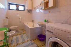 A small, clean bathroom with a toilet, sink, bathtub, and washing machine. - Apartment Ivka (Crikvenica)