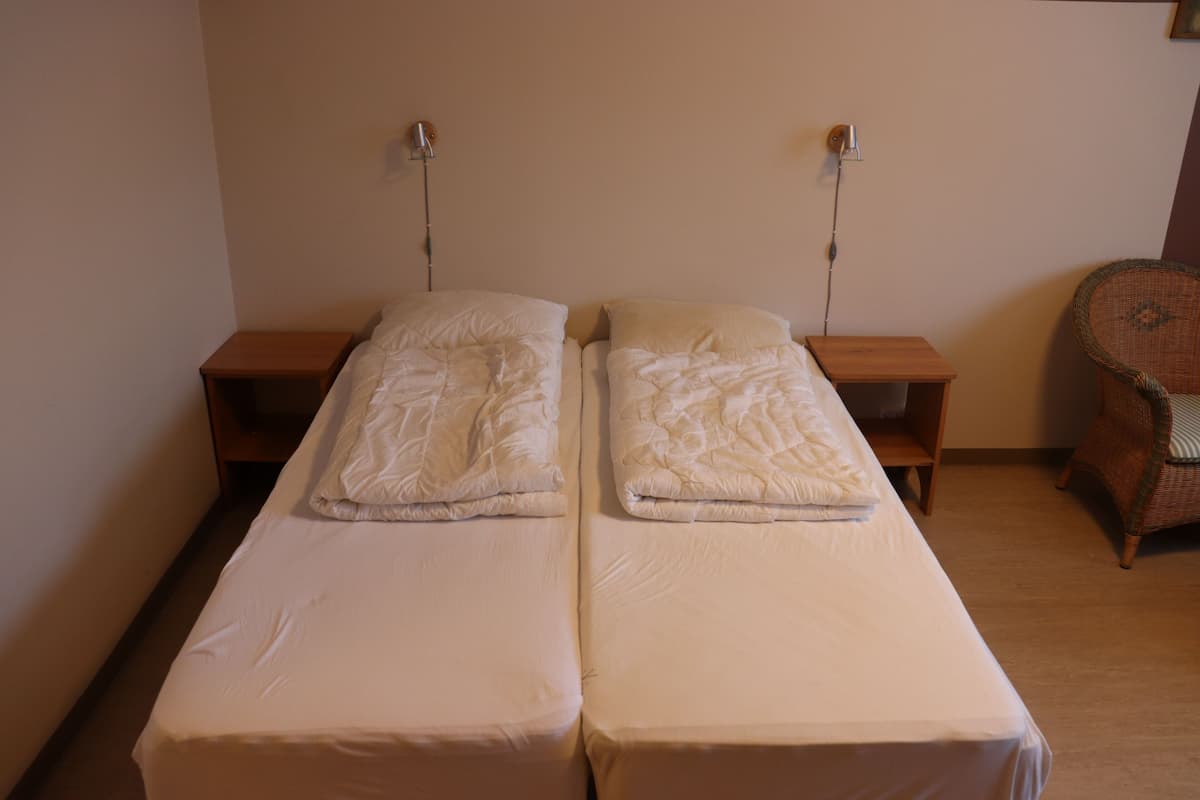 A twin room with two single beds, wooden nightstands, and a wicker chair.