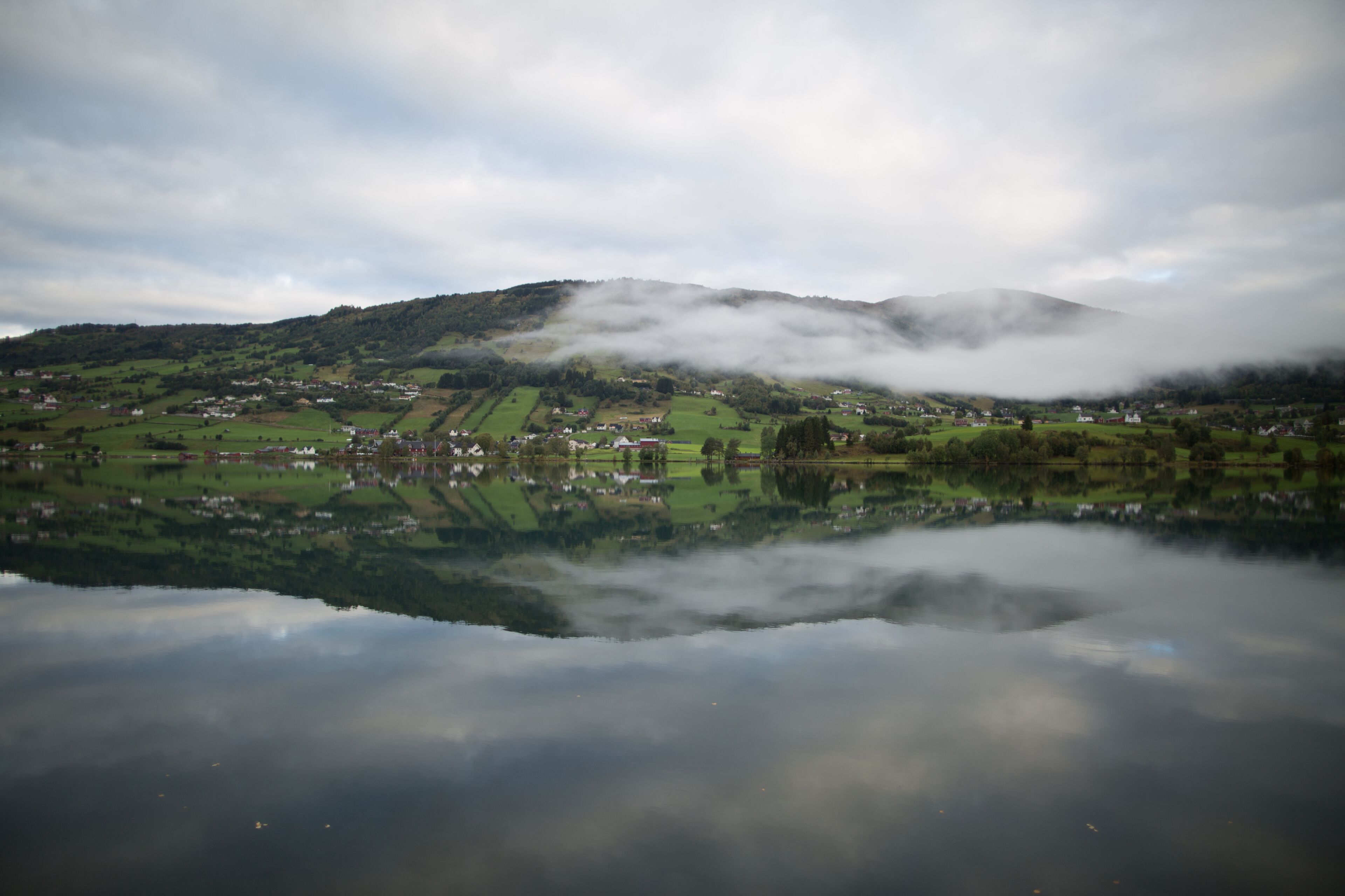 A calm lake reflecting a village with houses and a mountain in the background.