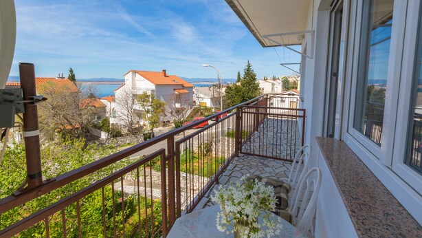 A balcony with a view of a coastal town, a table with a vase of flowers, and a railing. - Apartment Nada (Crikvenica)