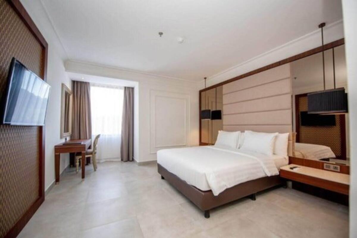 Habitación de hotel con una cama grande, un escritorio, una silla, un televisor y un espejo amplio.