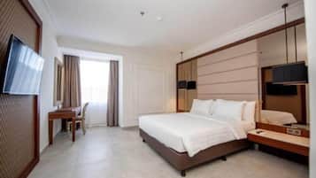 Quarto de hotel com uma cama grande, uma escrivaninha, uma cadeira, uma televisão e um espelho amplo.