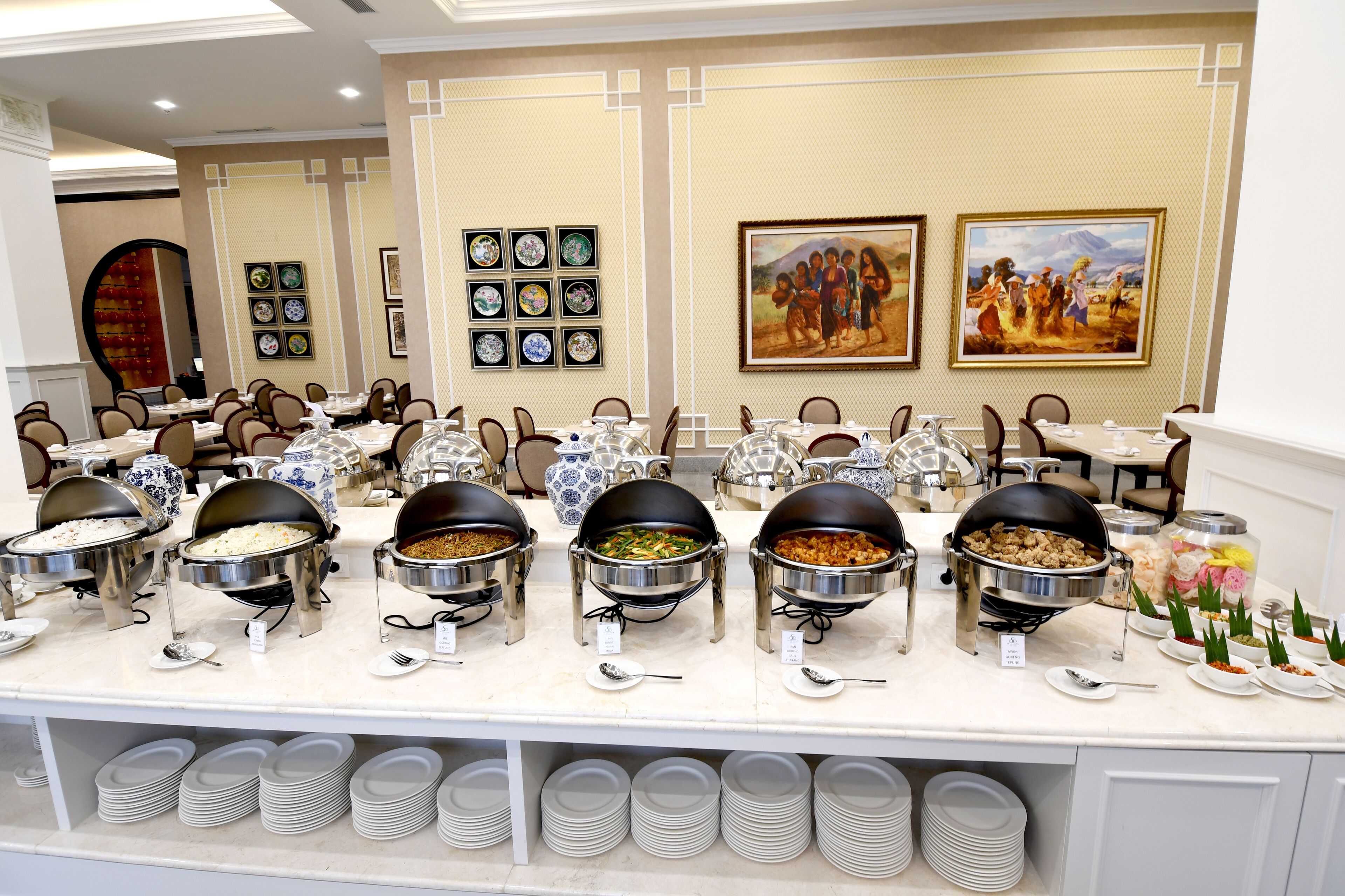 A buffet setup with multiple food stations, neatly arranged plates, and a wall decorated with framed artwork.