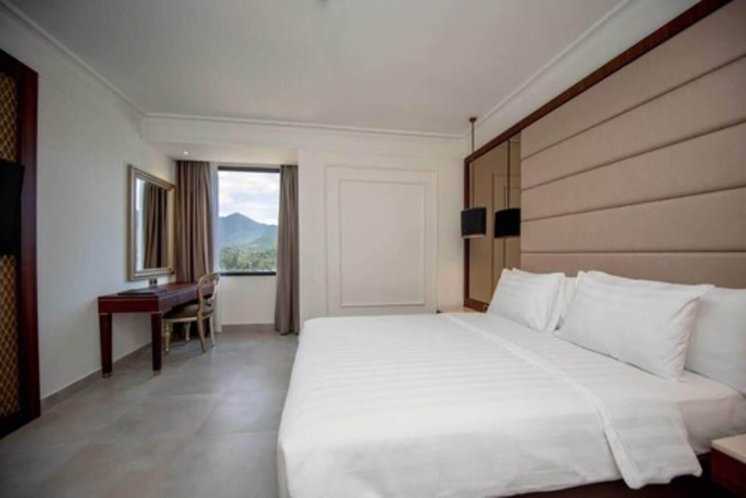 Ein Hotelzimmer mit einem großen Bett, einem Schreibtisch und einem Stuhl. Ein Fenster bietet Blick auf Berge.
