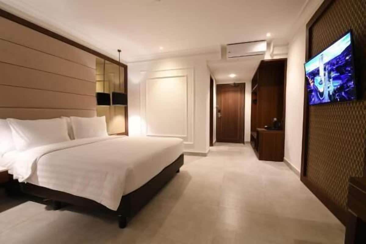 Habitación de hotel con cama, televisor, armario y puerta que da a otra habitación.