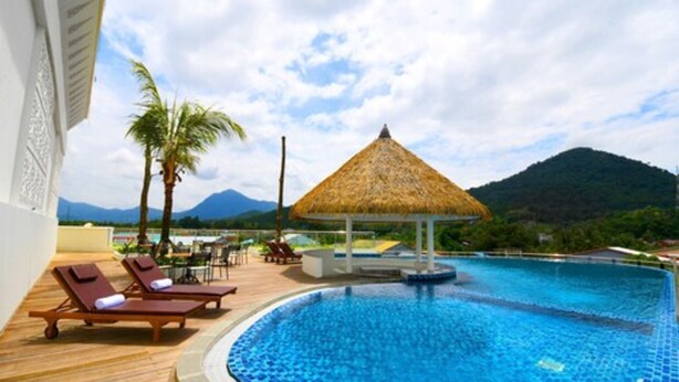 Zona de piscina con sillas de descanso y un pabellón de techo de paja, rodeada de palmeras y montañas.