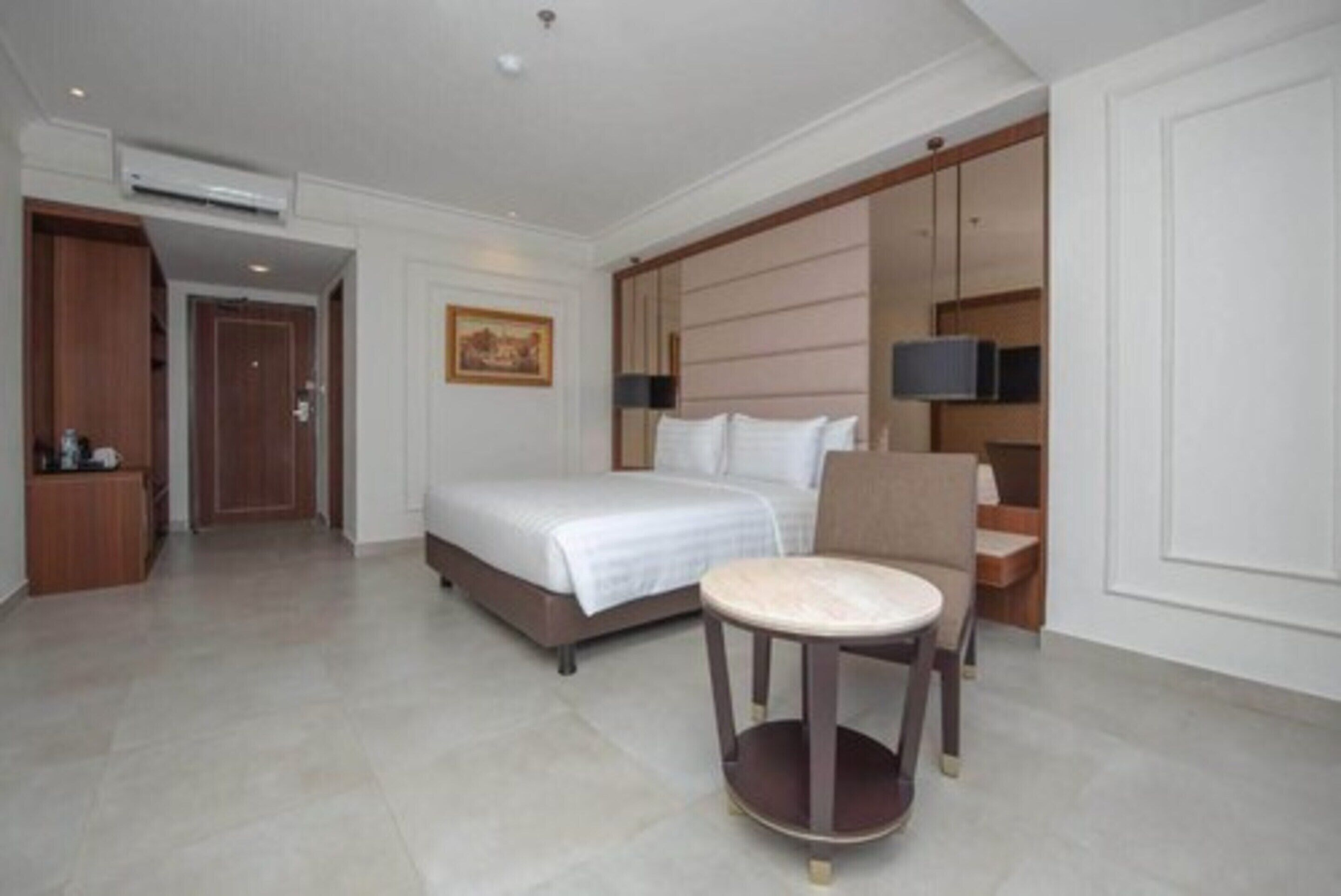 A hotel room with a bed, a round table, a chair, a TV, and a wardrobe.