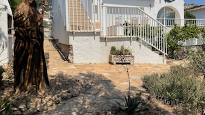 A white building with a staircase leading to a balcony, surrounded by plants and a stone pathway. - Ref. Mur16 -  (Rosas / Roses)