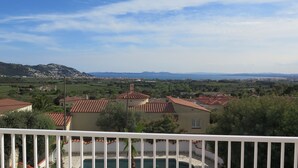 A residential area with terracotta-roofed houses, a swimming pool, and a view of distant mountains and a body of water. - Ref. Mur16 -  (Rosas / Roses)