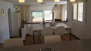 A modern dining area with a white table and chairs, a large window with a view, and pendant lighting. - Ref. Nav55 - (Rosas / Roses)