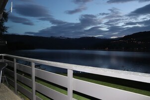 Vista para o lago com deck e grade de madeira, uma cadeia de montanhas ao longe e céu claro.
