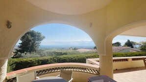 A covered outdoor seating area with a view of a landscape including trees and distant buildings.