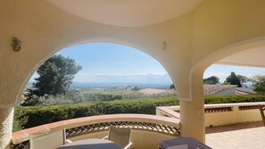 A covered outdoor seating area with a view of a landscape including trees and distant buildings.
