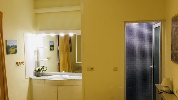 A hotel room with a bed, a bathroom with a sink and mirror, and a door leading to a tiled shower area.