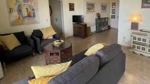 A living room with a sofa set, a coffee table, and a television. There is a bookshelf and a lamp in the room.