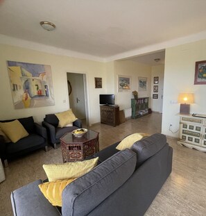 A living room with a sofa set, a coffee table, and a television. There is a bookshelf and a lamp in the room.