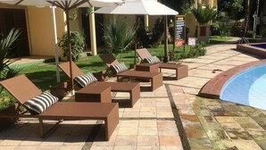 Een zwembadgedeelte met ligbedden en parasols, een betegeld terras en een bord met informatie over voorzieningen.