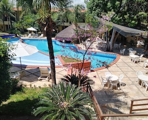 A pool area with lounge chairs and umbrellas, surrounded by lush greenery and a thatched-roof structure. - Chalet Solar Pipa (Tibau do Sul)
