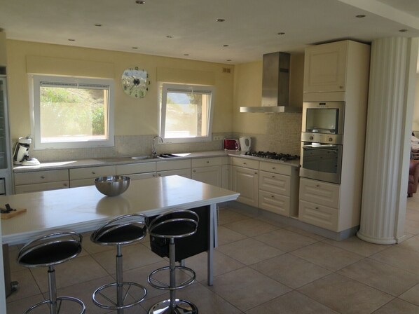 A modern kitchen with a central island, bar stools, a stove, oven, and a clock on the wall.