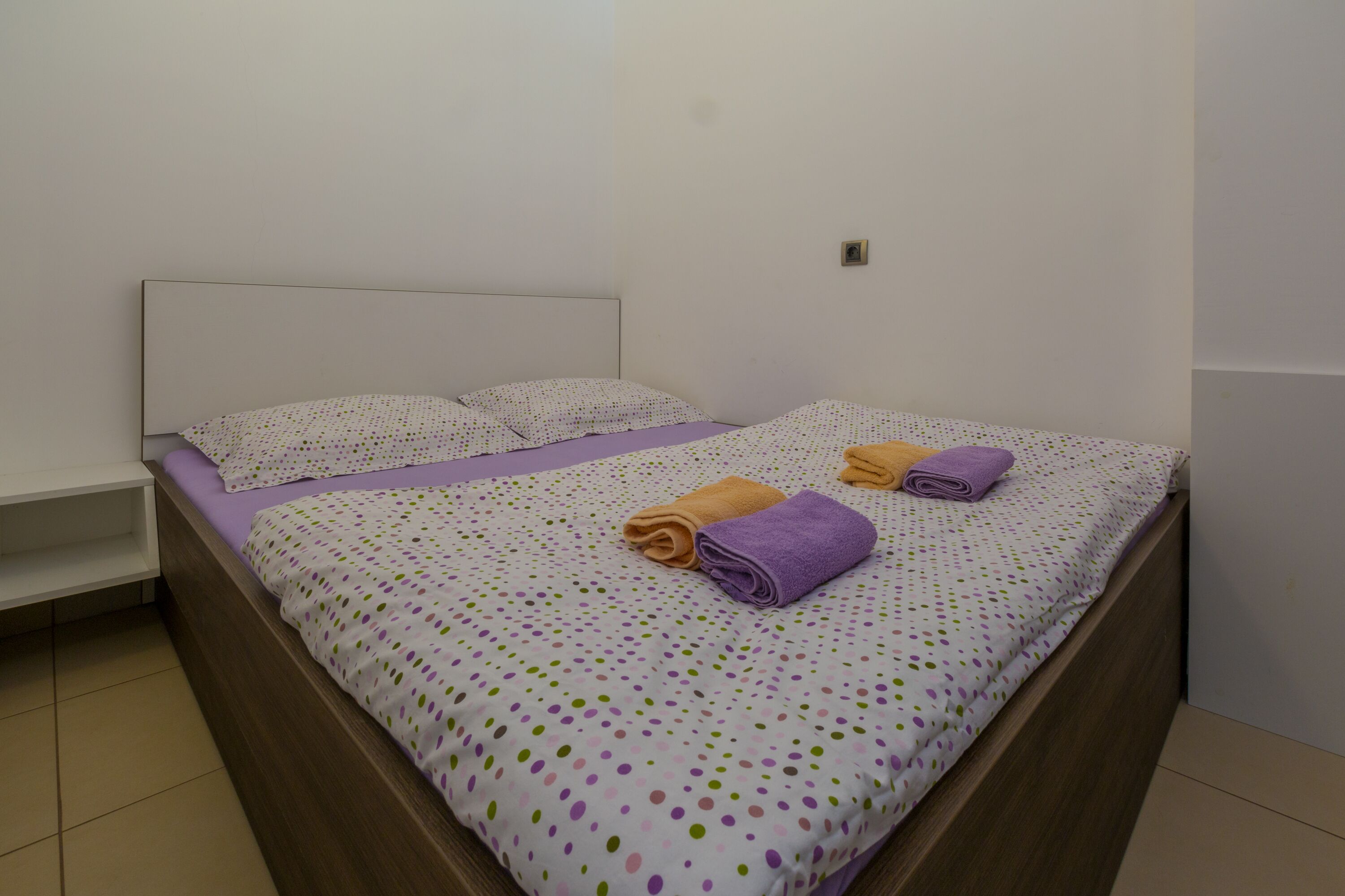 A neatly made bed with a polka dot bedspread, two pillows, and two rolled towels.