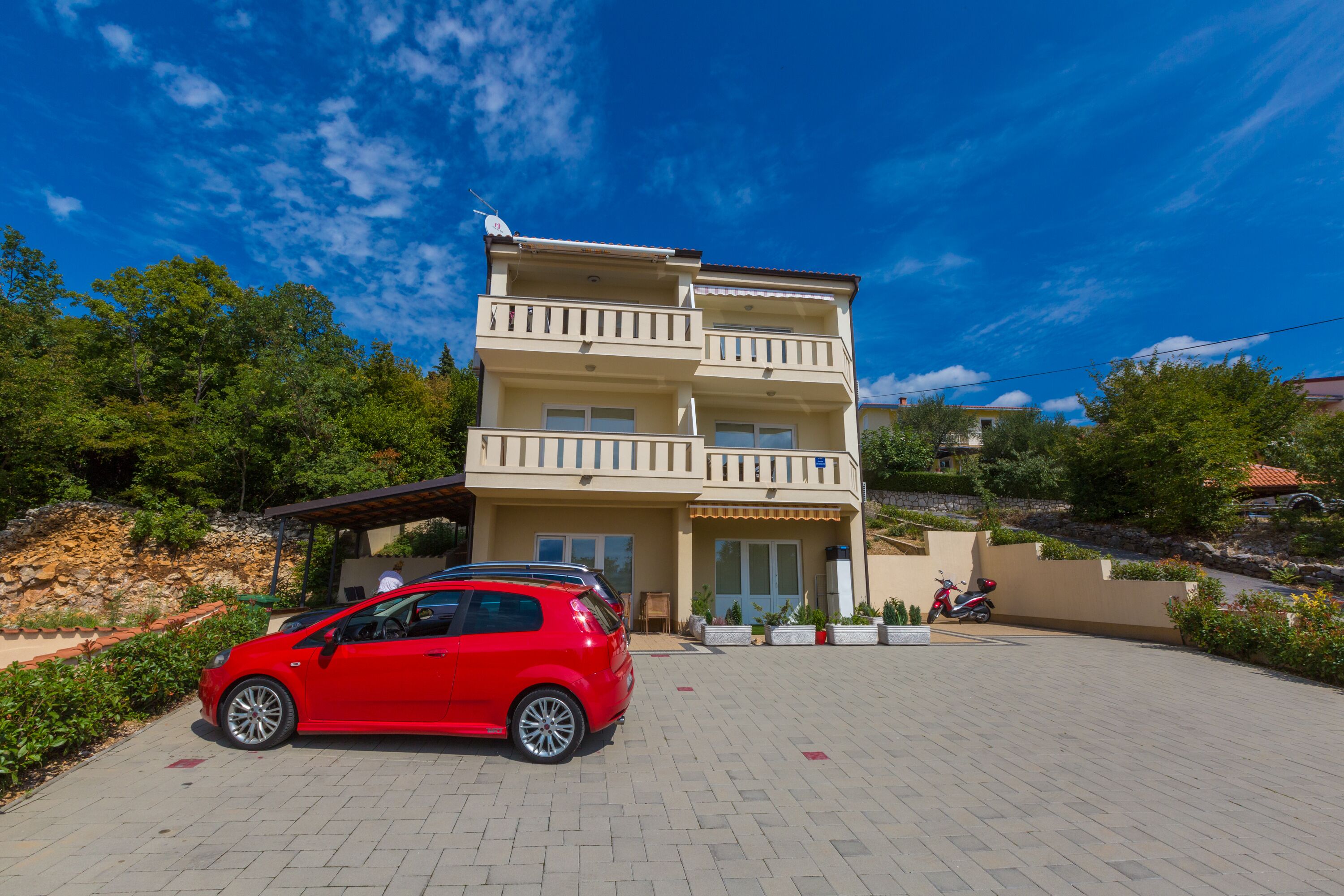 A multi-story building with a car and a scooter parked in front.