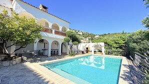 A pool with a stone deck, a white building with arches, and a hillside in the background. - Ref. Leo06 -  (Rosas / Roses)