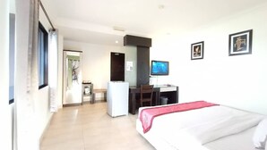 Habitación de hotel con cama, escritorio, silla, televisor y refrigerador.