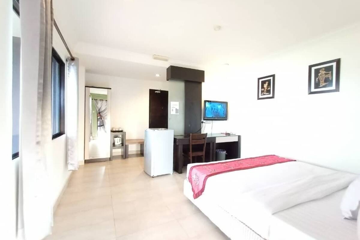 A hotel room with a bed, a desk, a chair, a television, and a refrigerator.