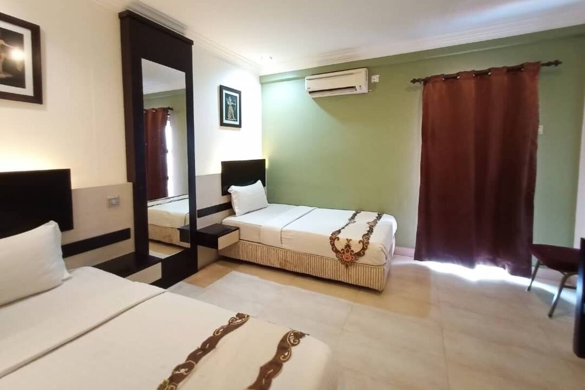 A hotel room with two beds, a large mirror, an air conditioner, and a view of the outside.