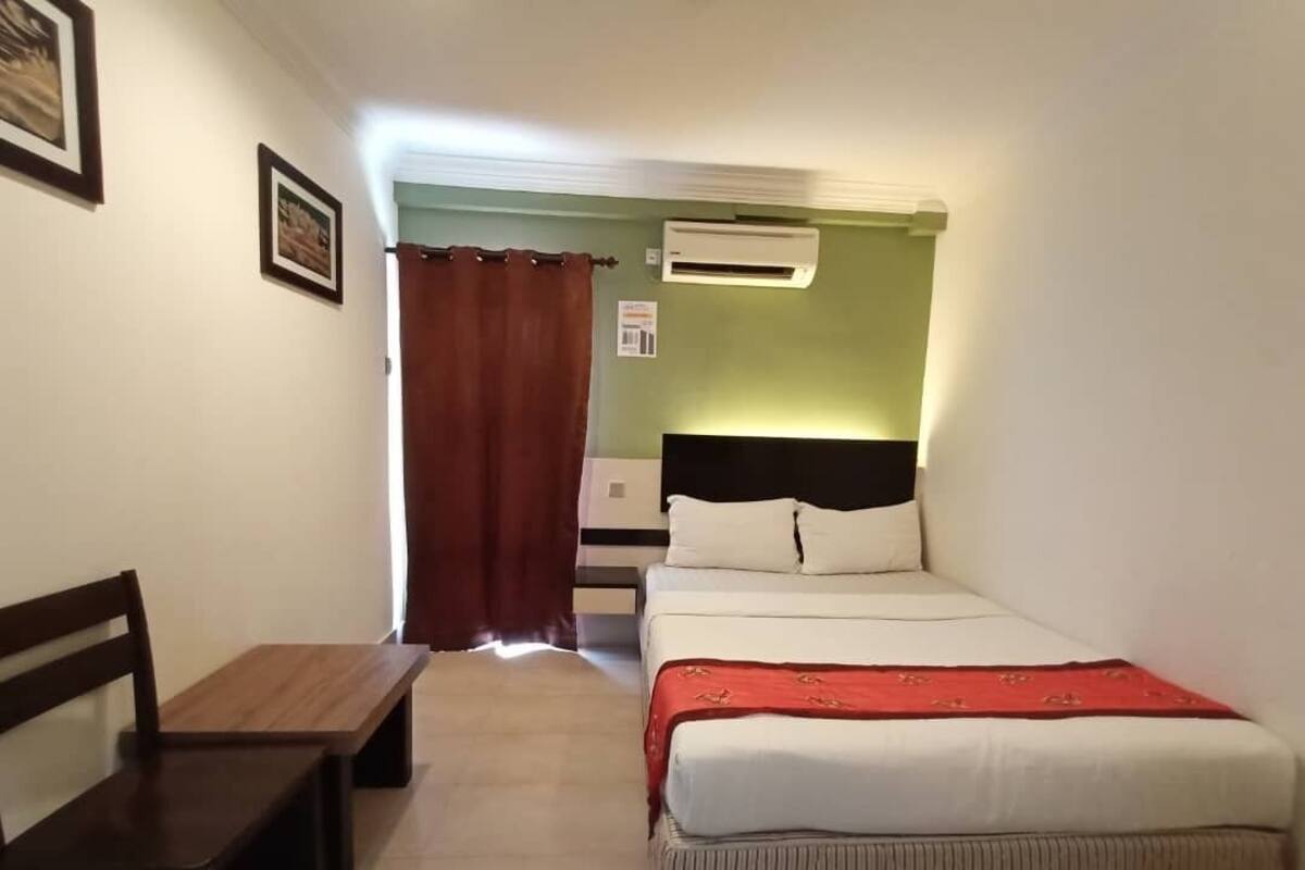 A bedroom with a bed, a wooden bench, an air conditioning unit, and a curtain.