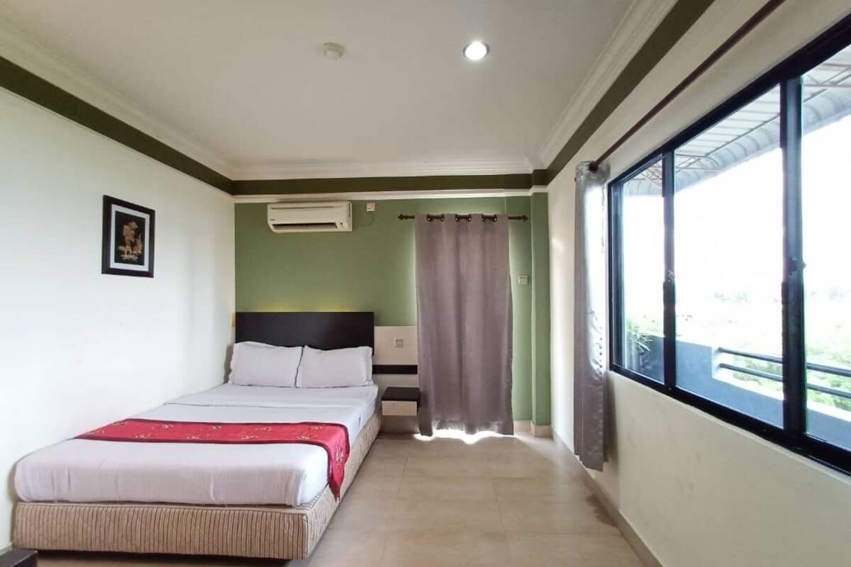 A hotel room with a bed, a window, and an air conditioning unit.