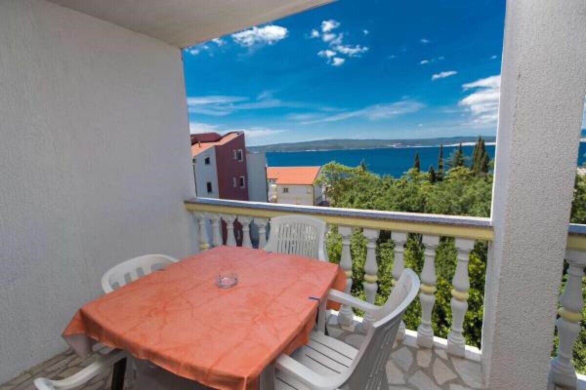 A balcony with a table and chairs, overlooking a coastal view with buildings and trees.
