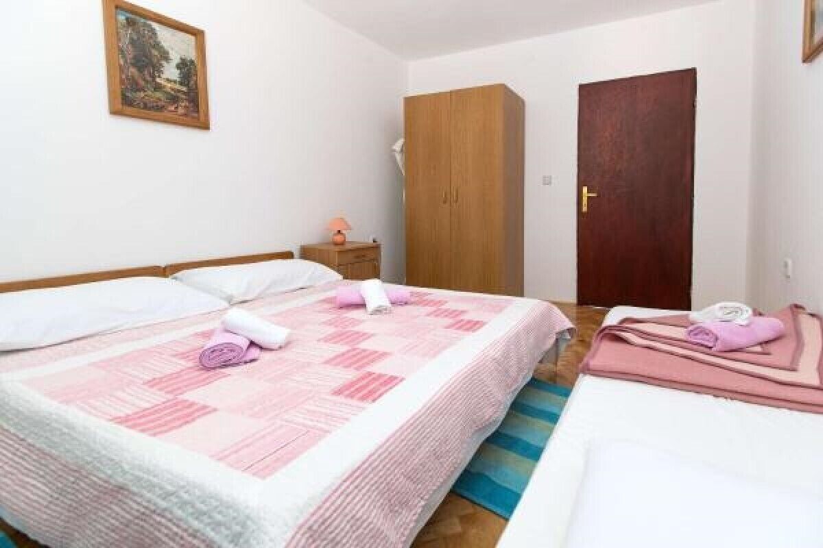 A bedroom with two beds, a wardrobe, a door, and a nightstand with a lamp.