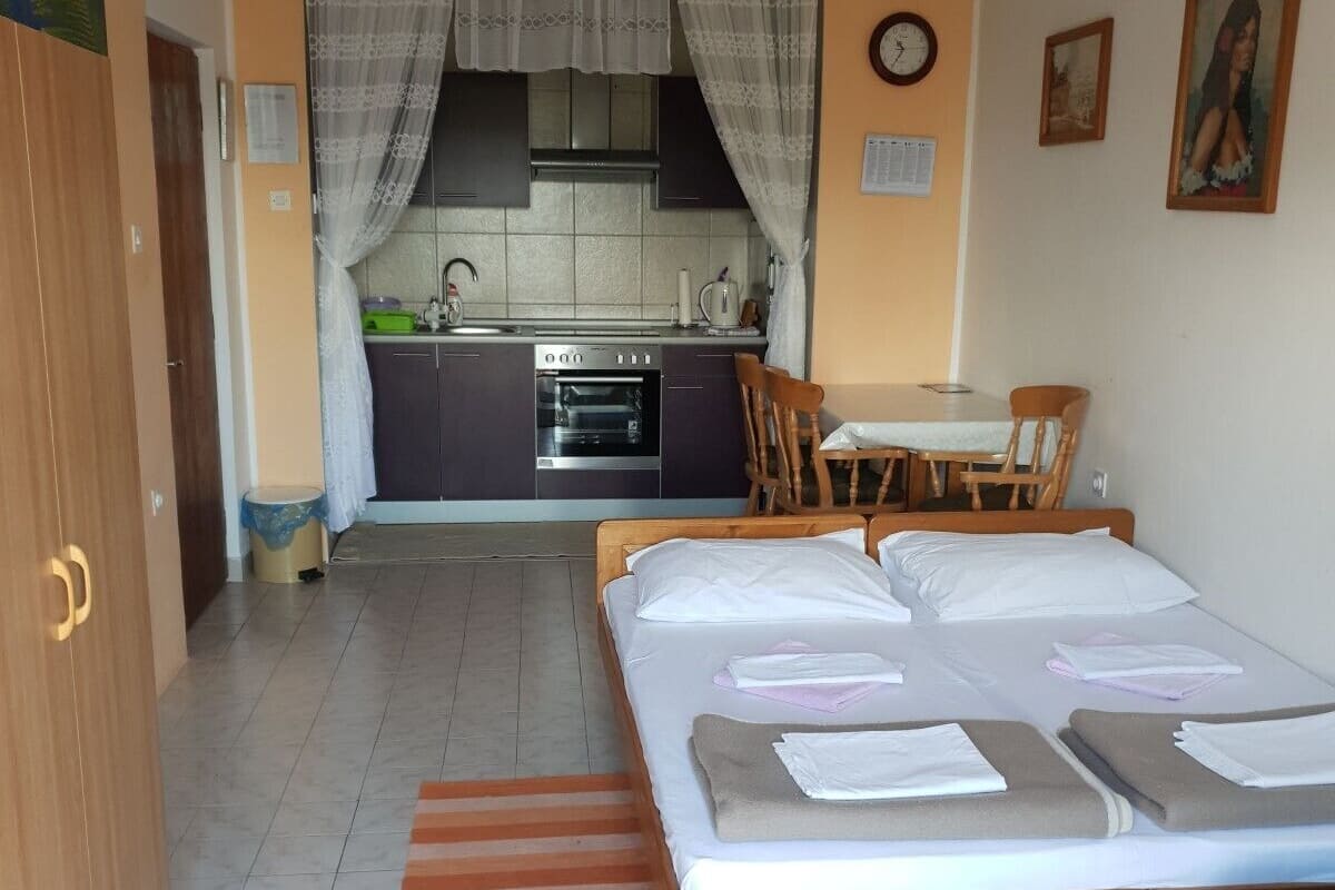 Quarto com cama, uma mesinha e uma kitchenette ao fundo.