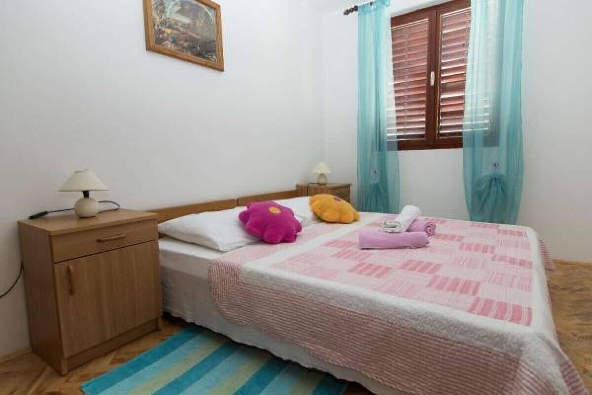 Quarto com cama, mesa de cabeceira, luminária, janela com cortinas e um quadro na parede.