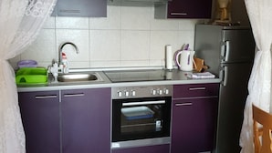 Una cocina compacta con armarios morados, un horno de acero inoxidable, un lavamanos y una cafetera.